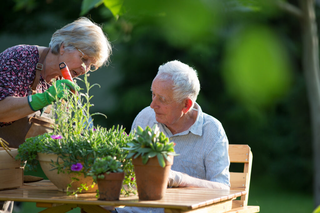 Couple sat at a table in the garden potting plants.