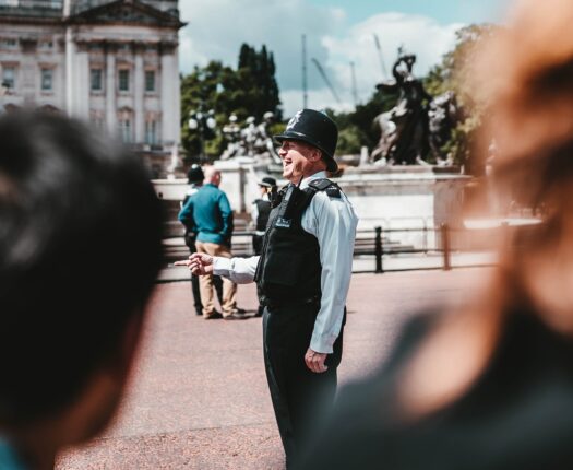 A laughing police officer in front of Buckingham Place, the image is slightly obscured by two people in the foreground.